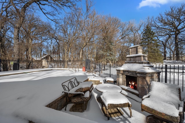 snow covered patio featuring an outdoor stone fireplace and fence