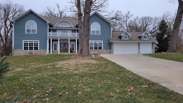 view of front of property featuring a front yard, stone siding, driveway, and an attached garage