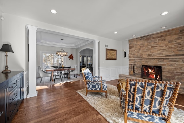 living area with dark wood-style floors, a wainscoted wall, crown molding, ornate columns, and a fireplace