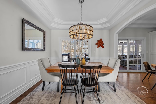 dining space featuring a wainscoted wall, wood finished floors, an inviting chandelier, a raised ceiling, and crown molding