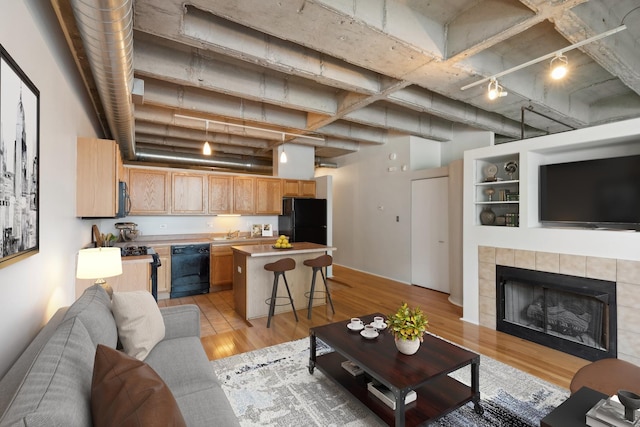 living room with a high ceiling, sink, light hardwood / wood-style flooring, and a tiled fireplace