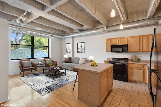 kitchen with a breakfast bar, a center island, black appliances, and light hardwood / wood-style floors