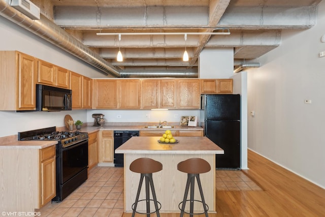 kitchen with a towering ceiling, sink, black appliances, light hardwood / wood-style floors, and a breakfast bar area