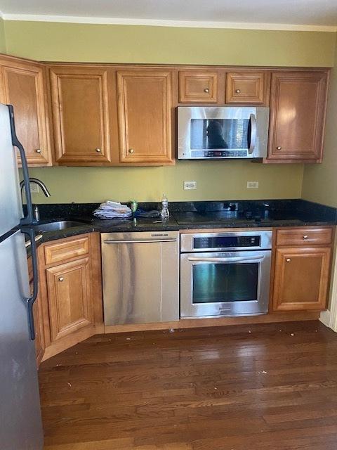 kitchen with sink, crown molding, dark stone countertops, stainless steel appliances, and dark hardwood / wood-style flooring