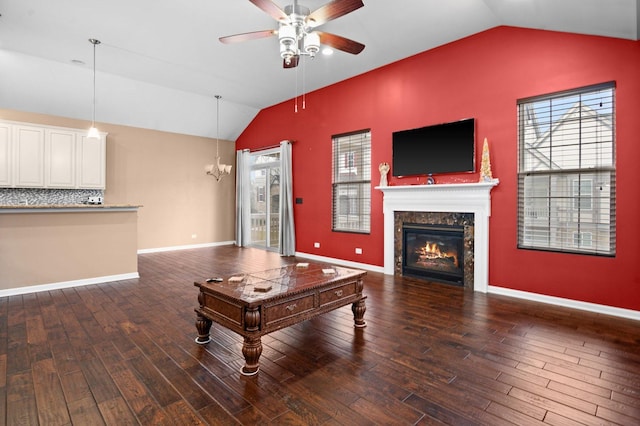 living room featuring ceiling fan with notable chandelier, dark hardwood / wood-style flooring, a premium fireplace, and vaulted ceiling