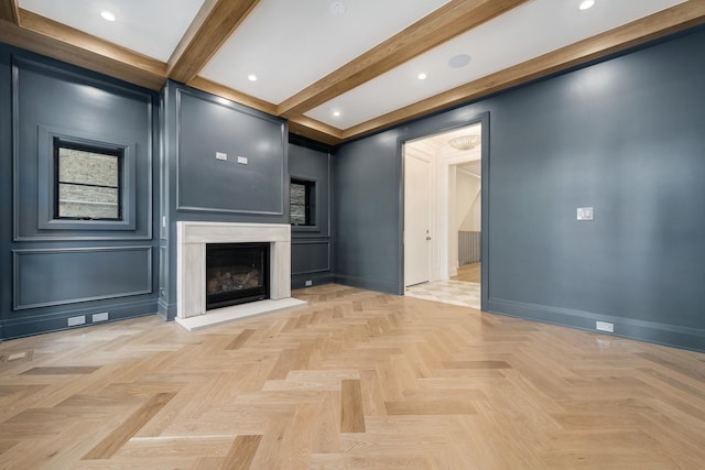 unfurnished living room with baseboards, a glass covered fireplace, a decorative wall, beam ceiling, and recessed lighting