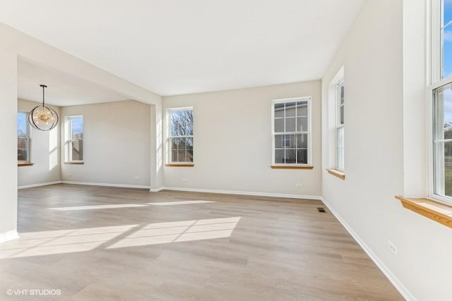 unfurnished room featuring a chandelier and light wood-type flooring