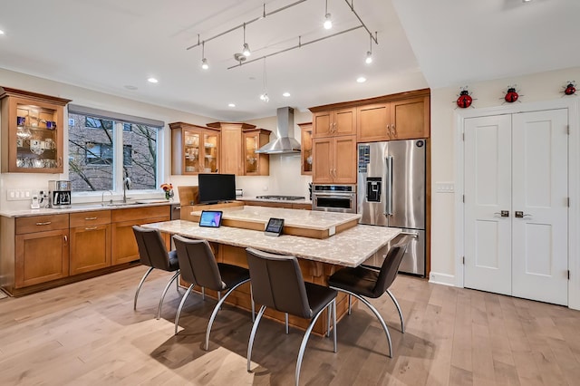 kitchen with sink, a center island, wall chimney exhaust hood, stainless steel appliances, and light hardwood / wood-style floors