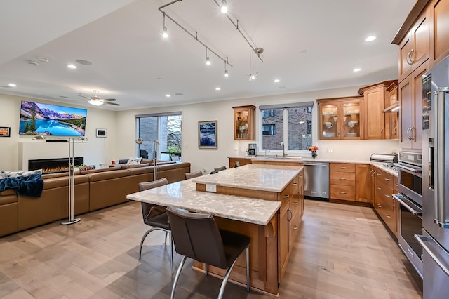 kitchen with ceiling fan, a center island, light stone countertops, stainless steel appliances, and a breakfast bar area