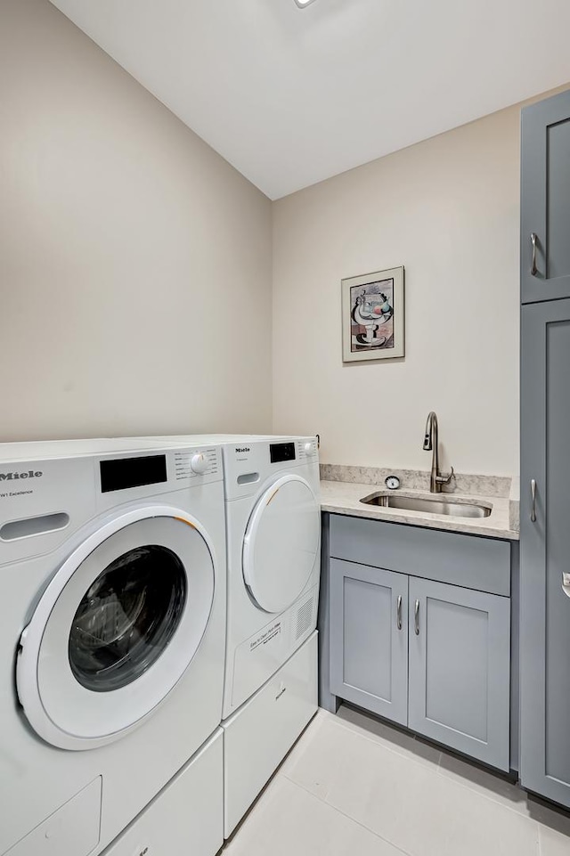 clothes washing area with washer and dryer, light tile patterned floors, cabinets, and sink