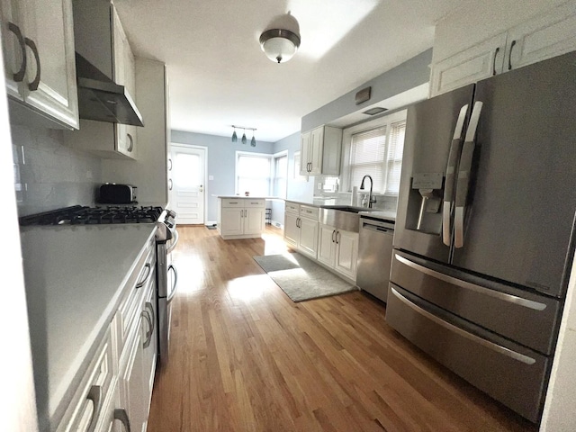 kitchen featuring white cabinets, sink, light hardwood / wood-style flooring, decorative backsplash, and appliances with stainless steel finishes