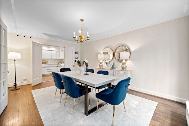 dining room featuring crown molding, light wood finished floors, an inviting chandelier, and baseboards