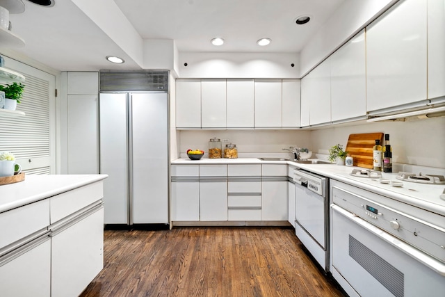 kitchen with dark wood-style floors, light countertops, white cabinetry, a sink, and white appliances