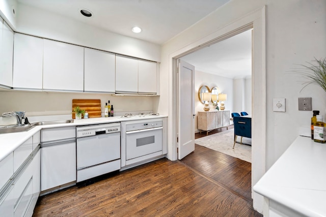 kitchen featuring dark wood-style floors, light countertops, white cabinets, a sink, and white appliances