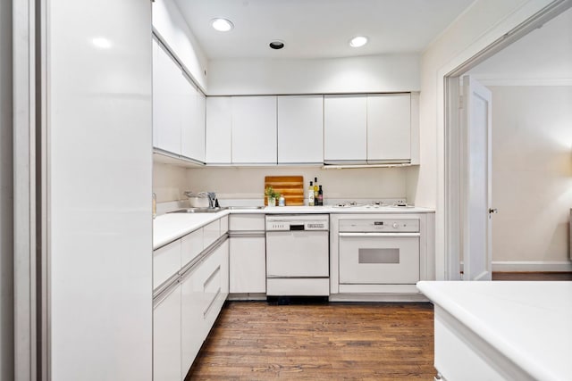 kitchen featuring dark wood-style flooring, light countertops, white cabinets, a sink, and white appliances