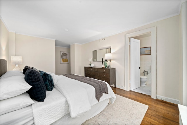 bedroom with ornamental molding, baseboards, ensuite bath, and wood finished floors