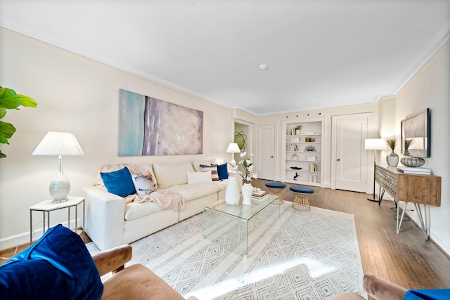 living room featuring built in shelves, crown molding, baseboards, and wood finished floors