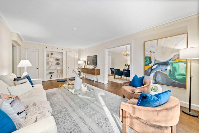 living room with a chandelier, built in shelves, wood finished floors, baseboards, and ornamental molding