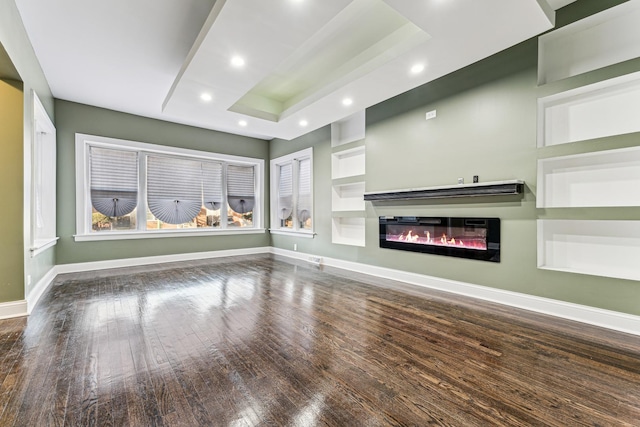 unfurnished living room with baseboards, a glass covered fireplace, wood finished floors, a tray ceiling, and recessed lighting