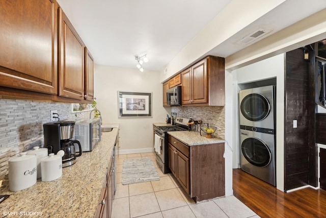 kitchen featuring appliances with stainless steel finishes, light stone counters, stacked washer / dryer, and light tile patterned flooring