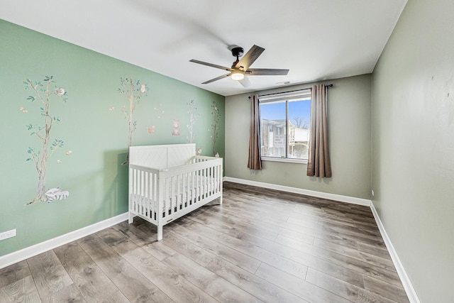 unfurnished bedroom with ceiling fan, wood-type flooring, and a crib