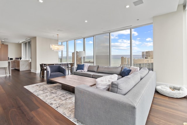 living room with a water view, an inviting chandelier, expansive windows, and dark wood-type flooring