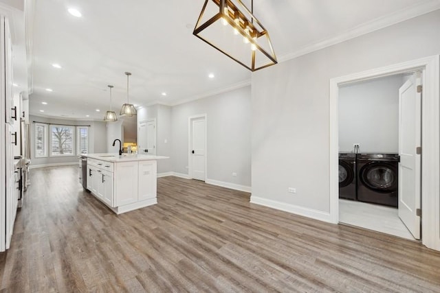 kitchen featuring washer and clothes dryer, crown molding, decorative light fixtures, a center island with sink, and light hardwood / wood-style floors