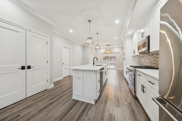 kitchen with backsplash, stainless steel appliances, sink, decorative light fixtures, and an island with sink