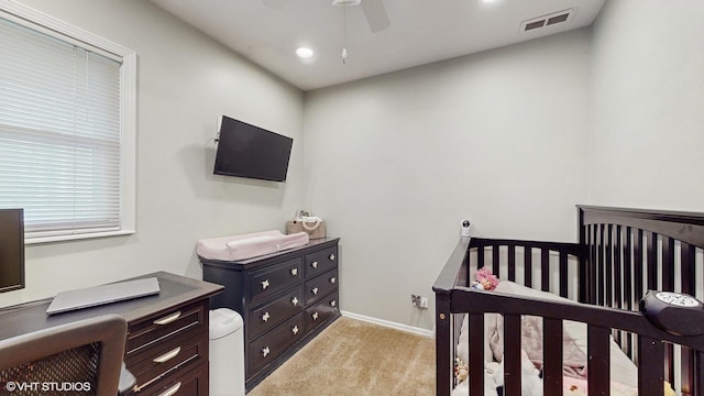 bedroom with ceiling fan, a nursery area, and light carpet