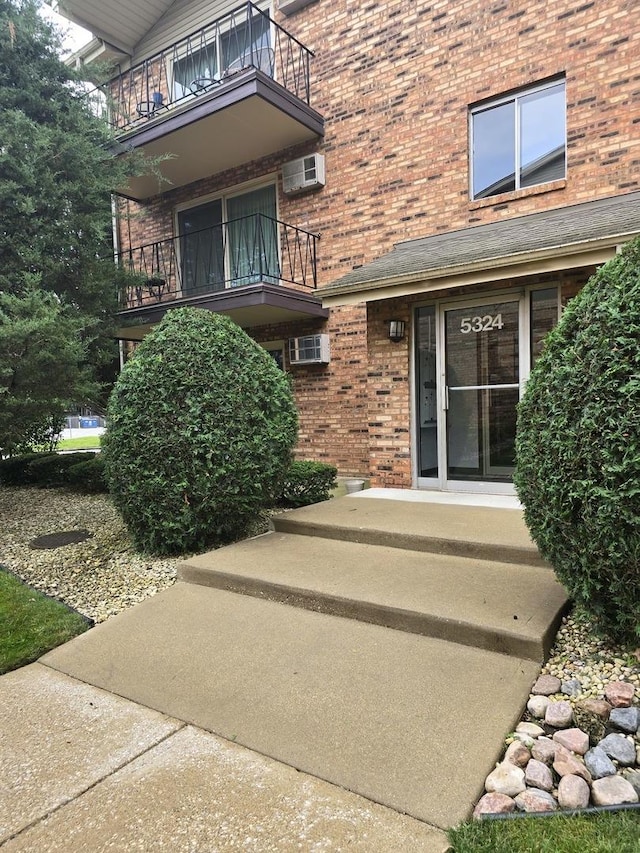 view of exterior entry featuring a balcony and a wall mounted AC