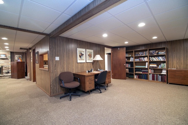 office with a drop ceiling, built in shelves, wooden walls, and carpet flooring