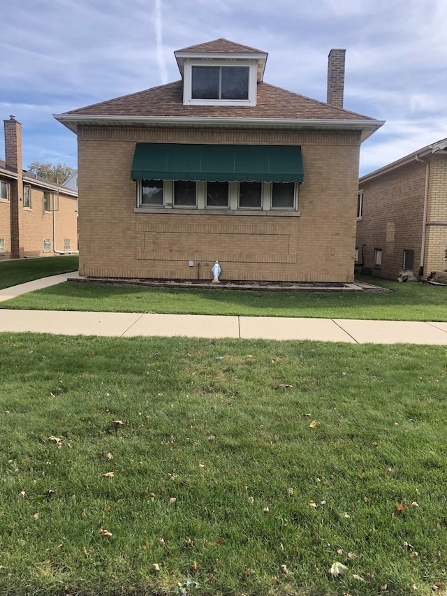 view of side of home with roof with shingles, brick siding, a lawn, and a chimney