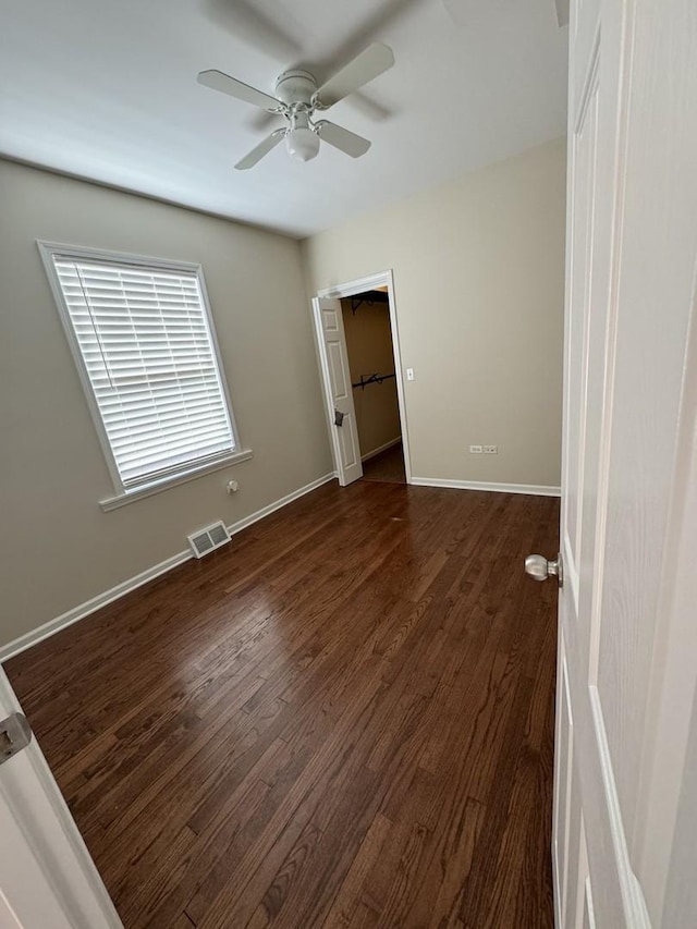 unfurnished bedroom with visible vents, baseboards, dark wood finished floors, a ceiling fan, and a spacious closet