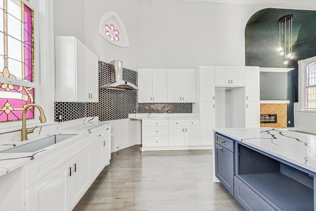 kitchen featuring white cabinetry, sink, light stone counters, and wall chimney range hood