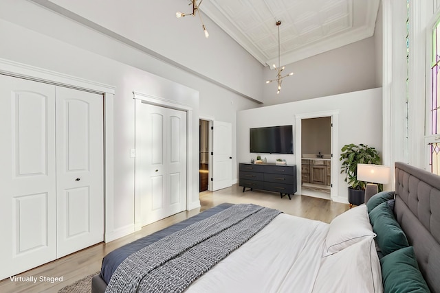 bedroom featuring connected bathroom, a towering ceiling, light wood-type flooring, and a notable chandelier