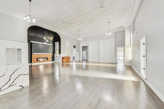 unfurnished living room featuring a brick fireplace, ornamental molding, a high ceiling, and light wood-type flooring