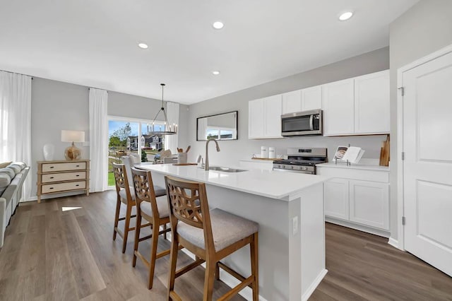 kitchen with appliances with stainless steel finishes, dark hardwood / wood-style flooring, sink, hanging light fixtures, and an island with sink