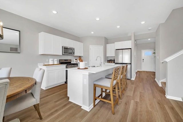 kitchen with sink, stainless steel appliances, a kitchen island with sink, white cabinets, and light wood-type flooring