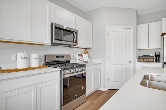 kitchen with light stone countertops, white cabinetry, light hardwood / wood-style floors, and appliances with stainless steel finishes