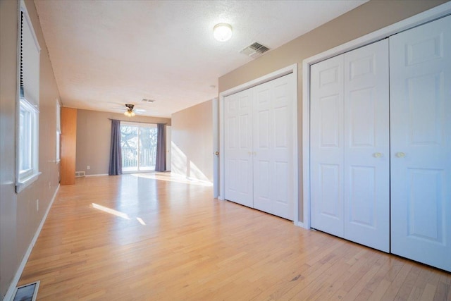 unfurnished bedroom with light hardwood / wood-style floors, a textured ceiling, and multiple closets