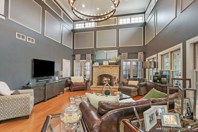 living room featuring a stone fireplace, a chandelier, light wood-type flooring, ornamental molding, and a high ceiling