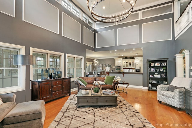 living room with decorative columns, a high ceiling, light hardwood / wood-style flooring, and a notable chandelier