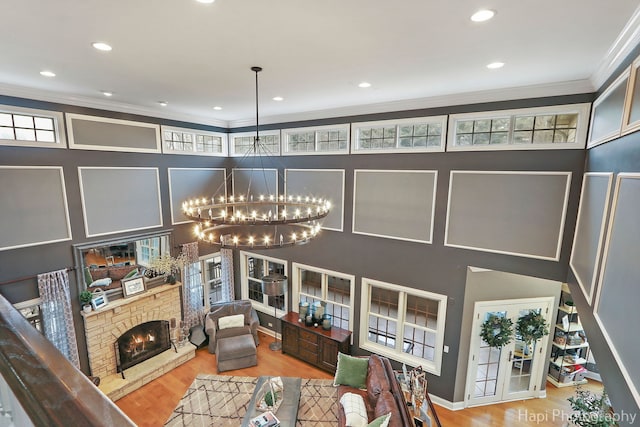 living room with hardwood / wood-style flooring, ornamental molding, a stone fireplace, and a notable chandelier