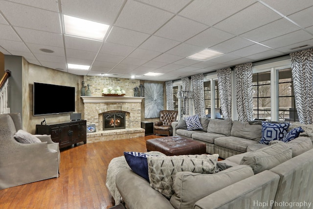 living room featuring wood-type flooring, a brick fireplace, and a drop ceiling