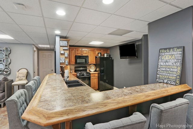 kitchen with sink, a breakfast bar area, a paneled ceiling, kitchen peninsula, and black appliances