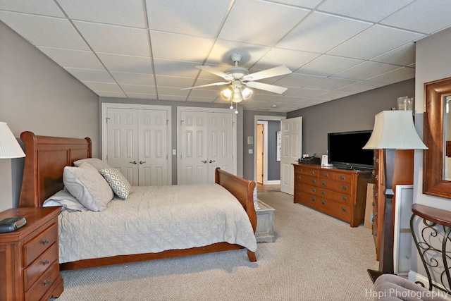 carpeted bedroom featuring a paneled ceiling, two closets, and ceiling fan