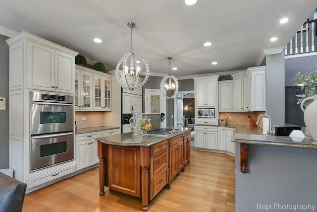 kitchen featuring appliances with stainless steel finishes, dark stone countertops, hanging light fixtures, white cabinets, and a kitchen island