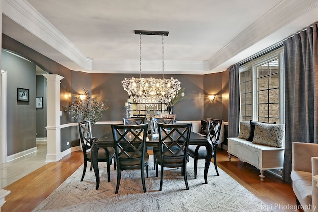 dining room with hardwood / wood-style flooring, ornamental molding, a raised ceiling, and ornate columns