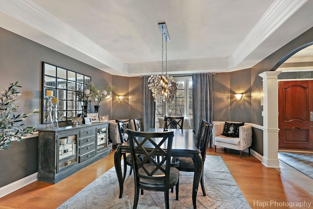 dining room with a notable chandelier, crown molding, wood-type flooring, and decorative columns