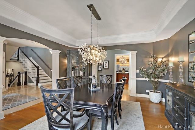 dining area with an inviting chandelier, ornamental molding, dark hardwood / wood-style flooring, a raised ceiling, and ornate columns